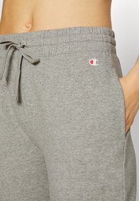 Gray cotton sweatpants with an elastic waistband, adjustable drawstring, side pockets, and a small logo on the thigh. Smooth texture.