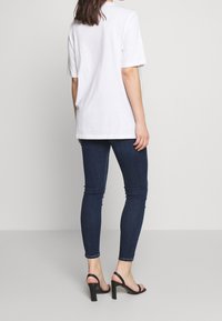 Camiseta de algodón blanca con mangas cortas, de corte relajado. Combinada con jeans ajustados de color azul oscuro y sandalias negras de tacón.