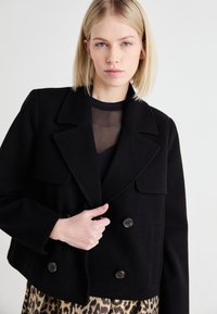 Melna īsā divrindas jaka ar lieliem atloka kabatām un divām priekšējām kabatām. Izgatavota no teksturēta auduma ar tumšām pogām un pielāgotu fit.
