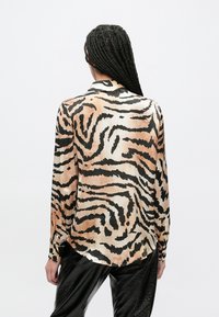 Pikad varrukad pluus kerge riidega, millel on beežide ja mustade tiigritriipude muster, kaardus äärega ja nööpidega mansettidega.