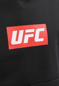 Tessuto nero con un rettangolo rosso al centro che presenta lettere bianche in grassetto del logo UFC.