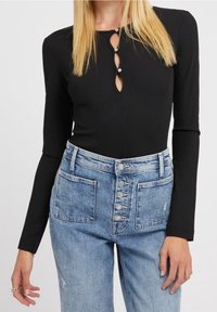 Zwarte geribde lange mouwen bodysuit met een keyhole halslijn, versierd met drie decoratieve knopen; gecombineerd met licht gewaste denim high-waisted jeans.