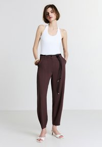 Body bianco a collo alto abbinato a pantaloni marroni a vita alta e svasati con coulisse nera e tasche. Il modello indossa mule bianche con tacco.