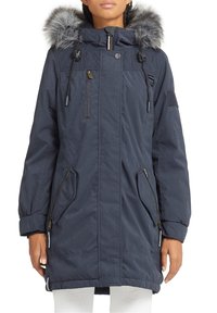 Tmavě modrá parka s kapucí lemovanou umělým kožešinou, zapínáním na zip vpředu a několika zipovými kapsami na bocích. Na ramenou prošívaná textura.