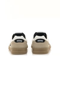 Zapatillas blancas y beige con acentos negros, que presentan un talón de ante texturizado y una suela de goma. El logo de la marca "mtng." está en la lengüeta del talón.
