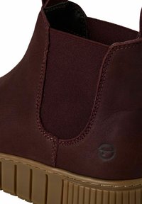 Burgundy ankle boot with elastic side panels, textured leather, and a ridged brown sole. Features a logo stamped on the side.