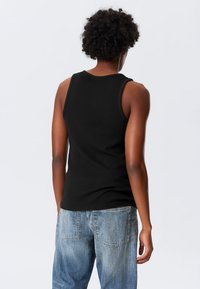 Crna majica bez rukava s uskim krojem, okruglim izrezom. Uparen sa svijetloplavim, širokim trapericama.