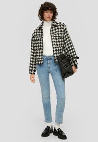 Jopica z vzorcem houndstooth v črni in beli barvi, bela rolka, svetlo modri jeans, črna prešita torbica, črni loaferji in bele nogavice.