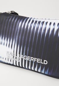 Pochette con zip bianco e nero con un motivo lineare, realizzata in tessuto morbido e con un'inconfondibile etichetta argento: "KARL LAGERFELD JEANS."