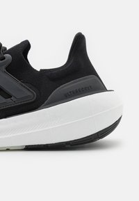 Sneaker nera con tomaia in mesh testurizzato, dotata di una robusta intersuola bianca e di una suola nera. Il lato mostra il marchio "ULTRABOOST".