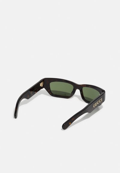 Occhiali da sole con montatura tartarugata, lenti verdi e logo "GUCCI" dorato sulla stecca. Design angolare con texture liscia.