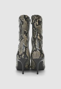 Stivaletti alla caviglia in stampa serpente nera e oro con silhouette affusolata, alti tacchi a spillo e texture in pelle lucida. Chiusura con zip sul retro.