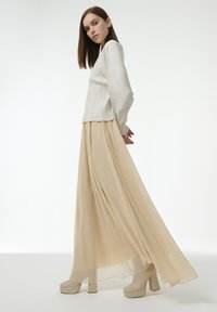 Haut à manches longues côtelé off-white associé à une longue jupe maxi beige fluide. Des chaussures à plateforme chunky de couleur beige clair complètent l'ensemble.