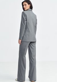 Szary garnitur w prążki z marynarką i spodniami o dopasowanym kroju, gładka tkanina, ostre klapy oraz detal mankietu z czterema guzikami. Obuwie w jasnym kolorze.