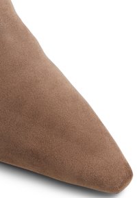 Scarpa in suede marrone con punta a forma allungata e texture liscia. Presenta un design elegante e una punta leggermente arrotondata, sottolineando un'eleganza minimalistica.