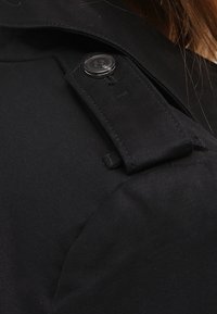 Tela negra con una superficie texturizada, que presenta un botón negro prominente y un detalle de correa, exhibiendo un diseño estructurado.