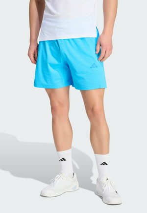 Pantaloncini sportivi blu con vita elasticizzata e logo. Abbinati a calzini bianchi alla caviglia e sneaker bianche con design testurizzato.