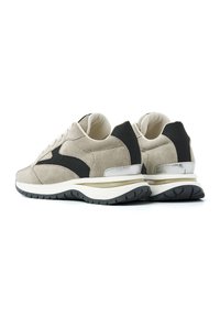 Beige Wildleder-Sneaker mit schwarzen Stoffakzenten, strukturierter Oberfläche, leichtem weißen Sohlen und dunkler Gummisohle für besseren Halt.