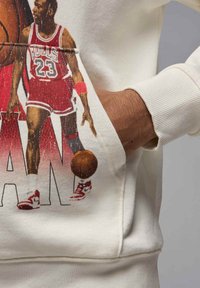 Kermansävyinen huppari, jossa on painatus koripalloilijasta punaisessa Bulls-uniformussa, punaiset yksityiskohdat ja etutasku.