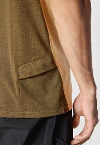 Olive green t-shirt with a brown side panel, featuring a small patch pocket. Soft texture and visible stitching detail.