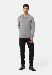 Grijze longsleeve polo met een kraag en drie knopen, gecombineerd met zwarte slim-fit broek en zwarte leren laarzen. Gladde textuur.