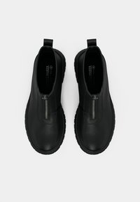 Μαύρες vegan δερμάτινες μπότες μέχρι τον αστράγαλο με κλείσιμο μπροστά με φερμουάρ, υφασμάτινη σόλα με υφή και λουράκια για εύκολη χρήση. Απαλός, μινιμαλιστικός σχεδιασμός.