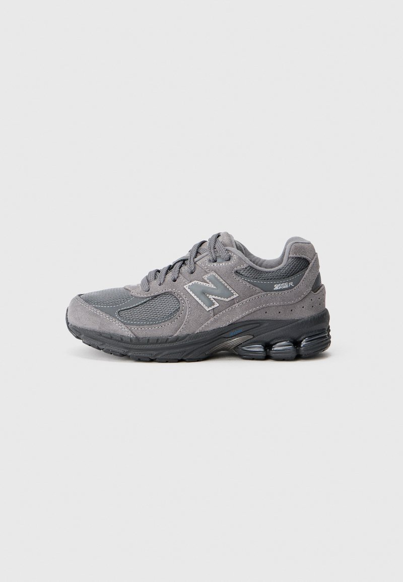 Pelēki sporta apavi ar strukturētu sieta un ādas augšdaļu; tiem ir mīkstināta zole un izcila New Balance logotipa zīme sānos.