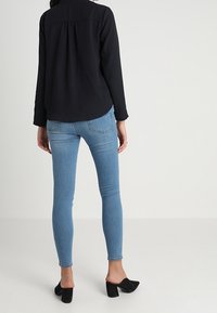 Blusa nera a maniche lunghe con un design a schiena arricciata, abbinata a jeans skinny blu chiaro e mule nere con tacco.