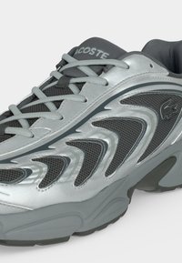 Baskets Lacoste grises et argentées avec panneaux en mesh, motif en zigzag, lacets et logo de la marque sur le côté et la languette.