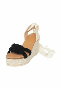 Cinture in tessuto nero con dettaglio a nodo, tacco a trapezio in paglia beige e soletta marrone chiaro. Laccetti bianchi attaccati al tallone per una calzata sicura.