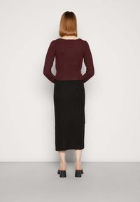 Sweater cropped canelado em bordeaux, com mangas longas, combinado com uma saia de malha preta, até ao joelho. Sapatos pretos com saltos robustos.