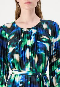 Vestido plissado com um padrão abstrato multicolorido em azul, verde e preto, com decote arredondado e um cinto combinando na cintura.