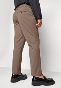 Bruna rutiga byxor med slim fit, bakfickor och matchat med glänsande svarta loafers med texturerad sula.