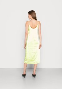 Vestido midi em cetim de cor verde limão vibrante. Apresenta alças finas ajustáveis e um decote nas costas em forma de U. Textura suave e silhueta ajustada.