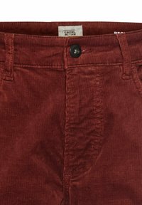 Rote Cord-Hosen mit glatter Textur, ausgestattet mit einem schwarzen Knopf, Gürtelschlaufen und einem Etikett am Bund, auf dem "camel active" steht.