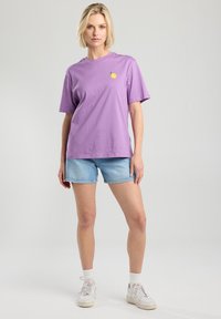 Purple cotton t-shirt with short sleeves, featuring a small yellow lemon graphic on the chest, paired with light blue denim shorts.