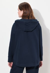 Marinblå huvtröja, mjuk textur, avslappnad passform, långa ärmar, ribbade muddar och fåll, med minimalistisk design och sömnadsdetaljer.