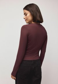 Burgunderfarbener Langarm-Top in einem glatten, figurschnitten Design, kombiniert mit hochgeschnittenen schwarzen Jeans und einem schlichten Rückenausschnitt.