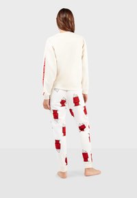 Sweatshirt crème à manches longues avec une accent rouge sur le côté ; associé à un pantalon de pyjama blanc à motifs carrés rouges. Texture douce.