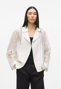 Veste de motard blanche transparente avec un motif texturé, une quincaillerie argentée et une fermeture éclair avant. Manches longues et col classique.