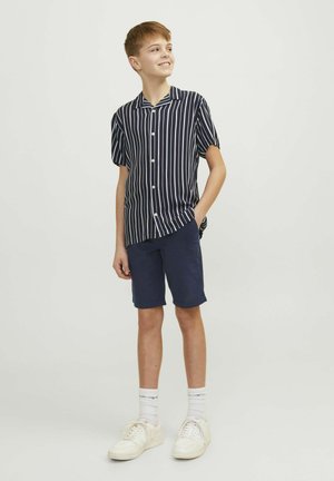 Marinblå och vitrandig kortärmad skjorta med knappar, tillsammans med marinblå shorts och vita sneakers. Slät tygkvalitet och avslappnad passform.
