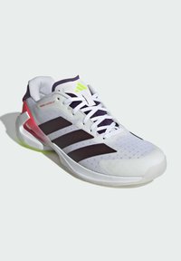 Chaussure de sport Adidas noire et blanche avec un logo vert fluo, un support de talon rouge, des lacets blancs et une tige en mesh, inclinée pour montrer les détails latéraux et frontaux.