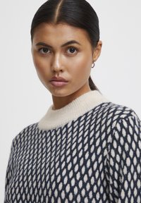 Maglione a motivo navy e crema con una morbida texture lavorata a maglia e colletto a coste crema, caratterizzato da un design a forma di diamante su tutta la superficie.