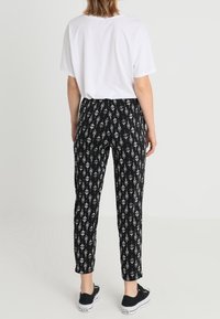 Schwarze gemusterte Hose mit einem weißen geometrischen Design, im entspannten Schnitt und mit schmal zulaufenden Beinen, kombiniert mit einem schlichten weißen T-Shirt und schwarzen Sneakern.