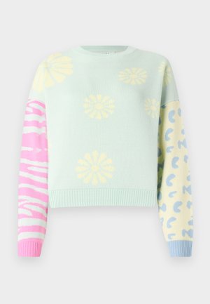 Pull court bleu clair avec des imprimés de fleurs jaunes sur le devant, des rayures zébrées roses et blanches sur la manche gauche, des taches de léopard bleues sur la manche droite.