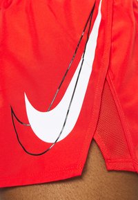 Shorts de sport rouges avec un grand logo Nike swoosh blanc. Confectionnés en tissu lisse avec des panneaux latéraux en mesh pour la ventilation.