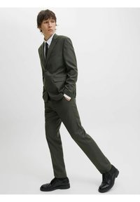 Oliven grøn jakkesæt med en enkeltstående knap blazer, matchende bukser, hvid skjorte og sort slipse. Sorte sko med en tekstureret finish.