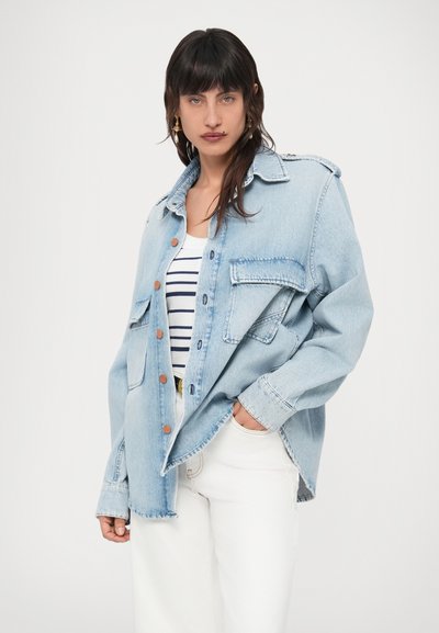 Φωτεινή γαλάζια τζιν μπουφάν με χαλαρή εφαρμογή, με μπροστινές τσέπες, πορτοκαλί κουμπιά και ξεφτισμένο τελείωμα. Φορεμένο πάνω από ριγέ αμάνικη μπλούζα.