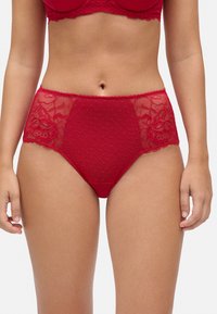 Bragas rojas de talle alto con un patrón de lunares, detalles de encaje y bordes ondulados en la cinturilla y las piernas.