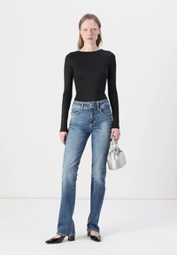 Black long-sleeve bodysuit with silver embellishments, light blue straight-leg jeans, and a small silver handbag. Black patent shoes with bows.